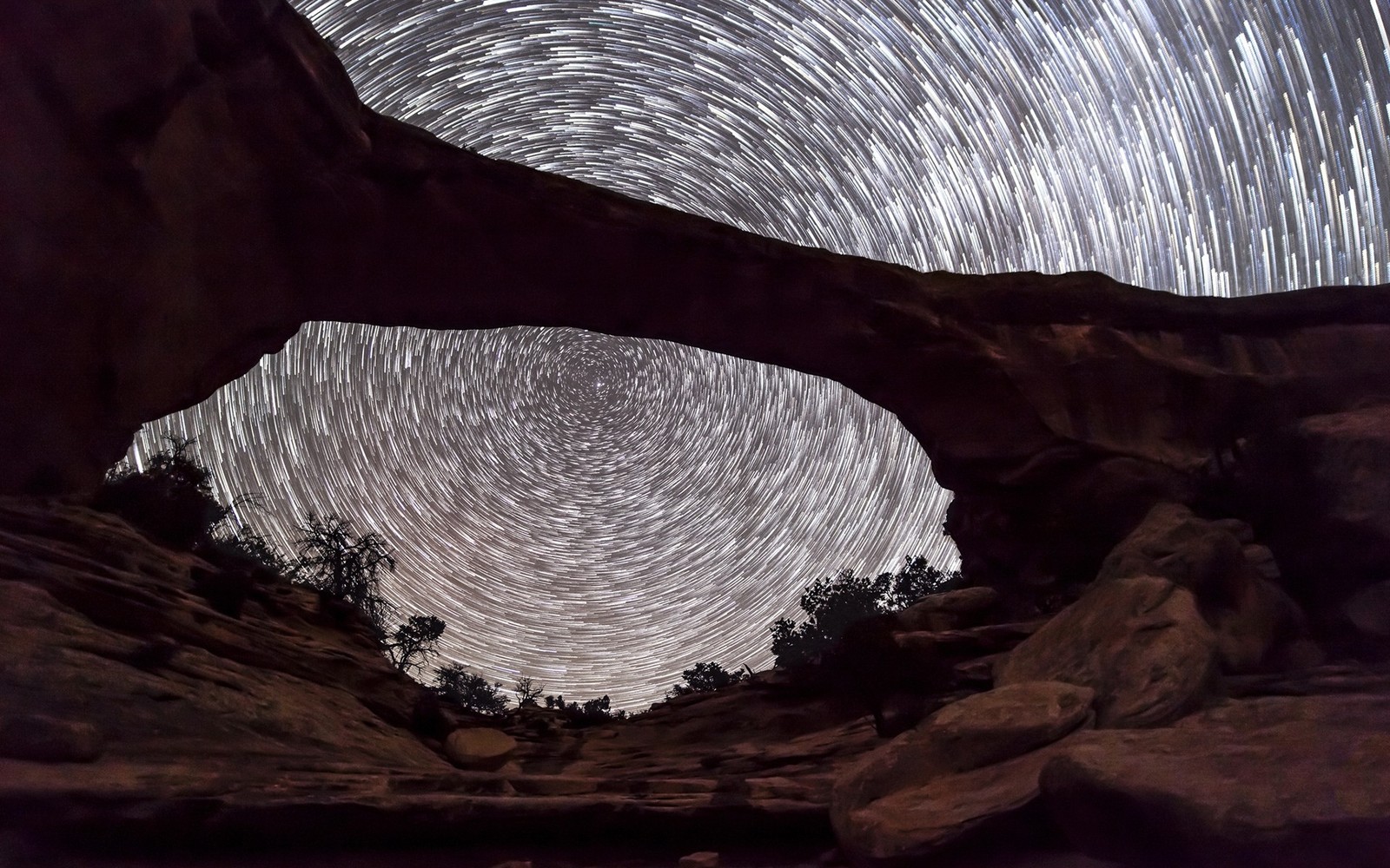 A view of a rock arch with a star trail in the sky (night, natural arch, national park service, canyonlands national park, sky)