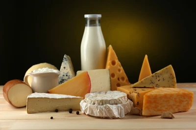 Un agencement diversifié de produits laitiers, y compris divers fromages, du lait et du yaourt, présenté dans une composition de nature morte.