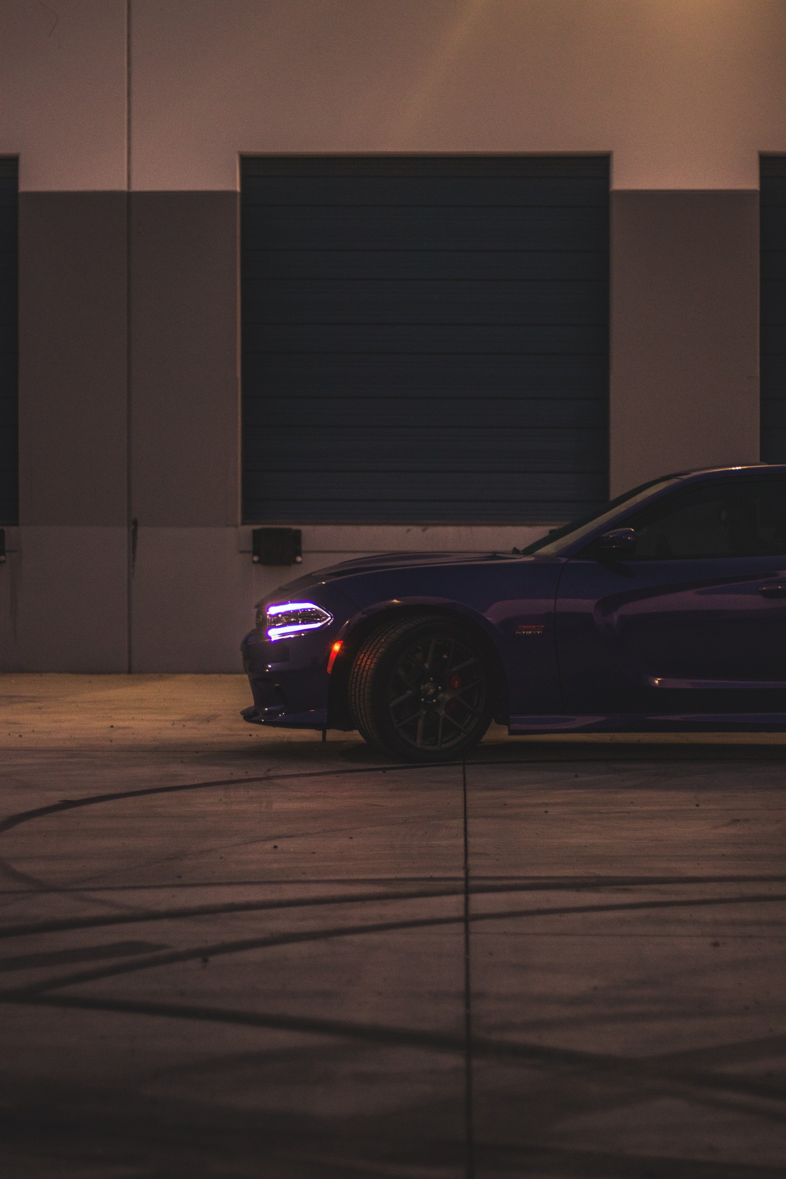 Une voiture violette garée sur un parking la nuit avec les lumières allumées (voiture, jante, roue, pneu, berline)