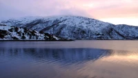 Montanhas cobertas de neve se refletem em um fiorde tranquilo ao pôr do sol.