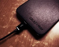 Smartphone Galaxy Note con cable de carga USB sobre superficie de madera