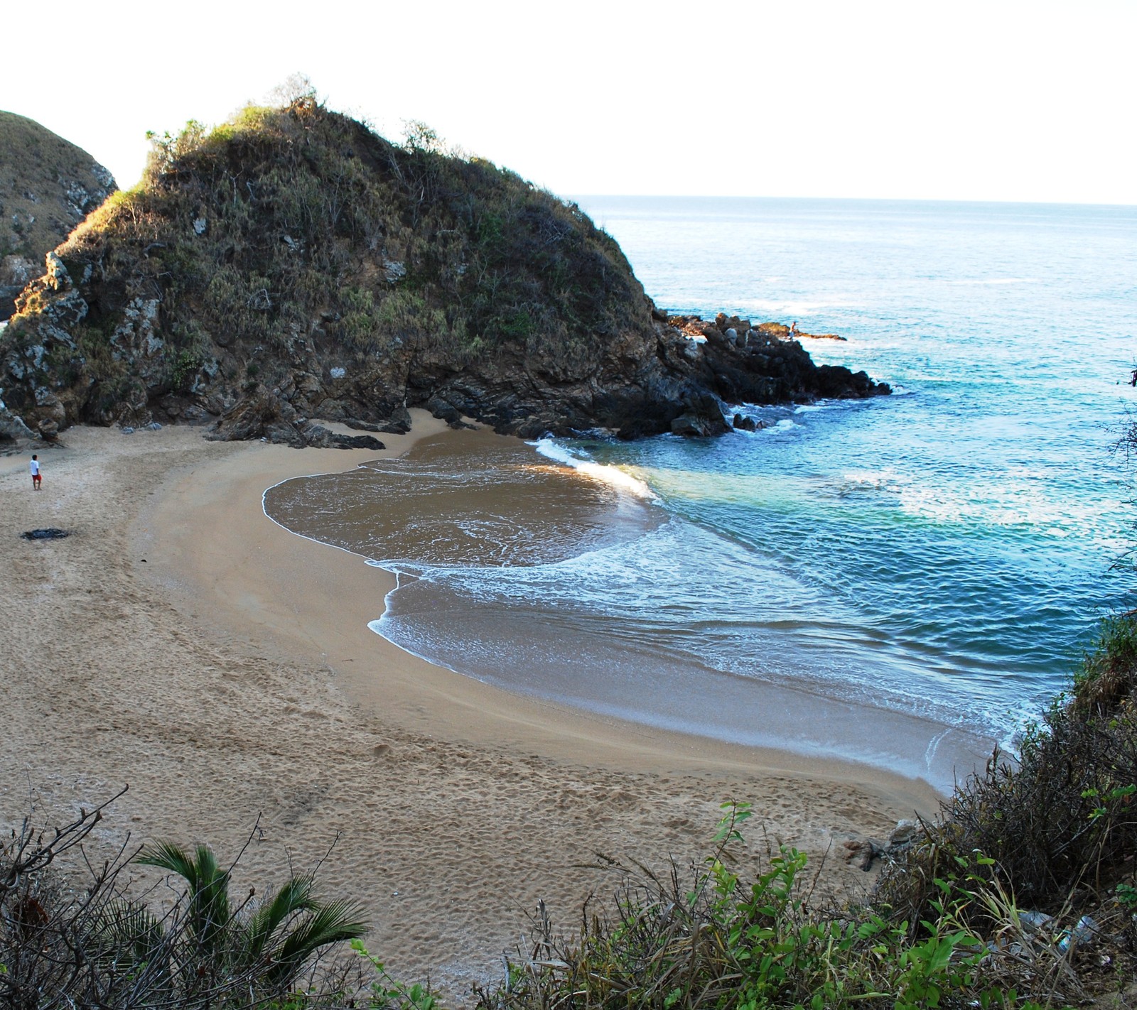 Hay una playa de arena con una pequeña colina al fondo (mar, méxico, oaxaca, playa, playa zipolite)