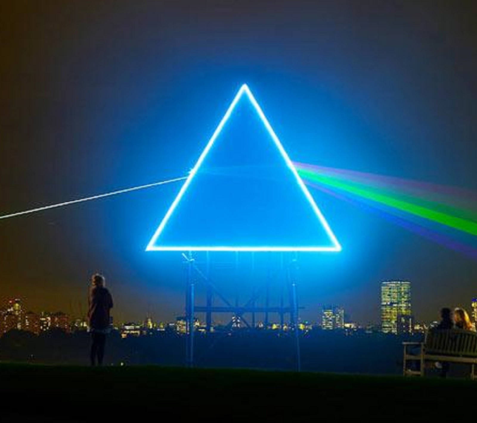 Una vista aérea de un hombre de pie frente a un gran triángulo (lado oscuro de la luna, pink floyd)