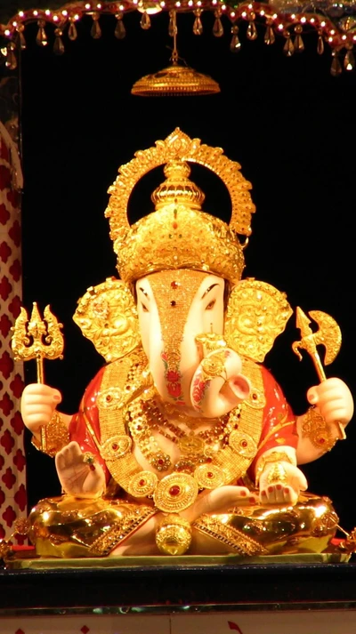 Golden idol of Lord Ganesha adorned with intricate jewelry, seated in a traditional pose, radiating devotion and auspiciousness.