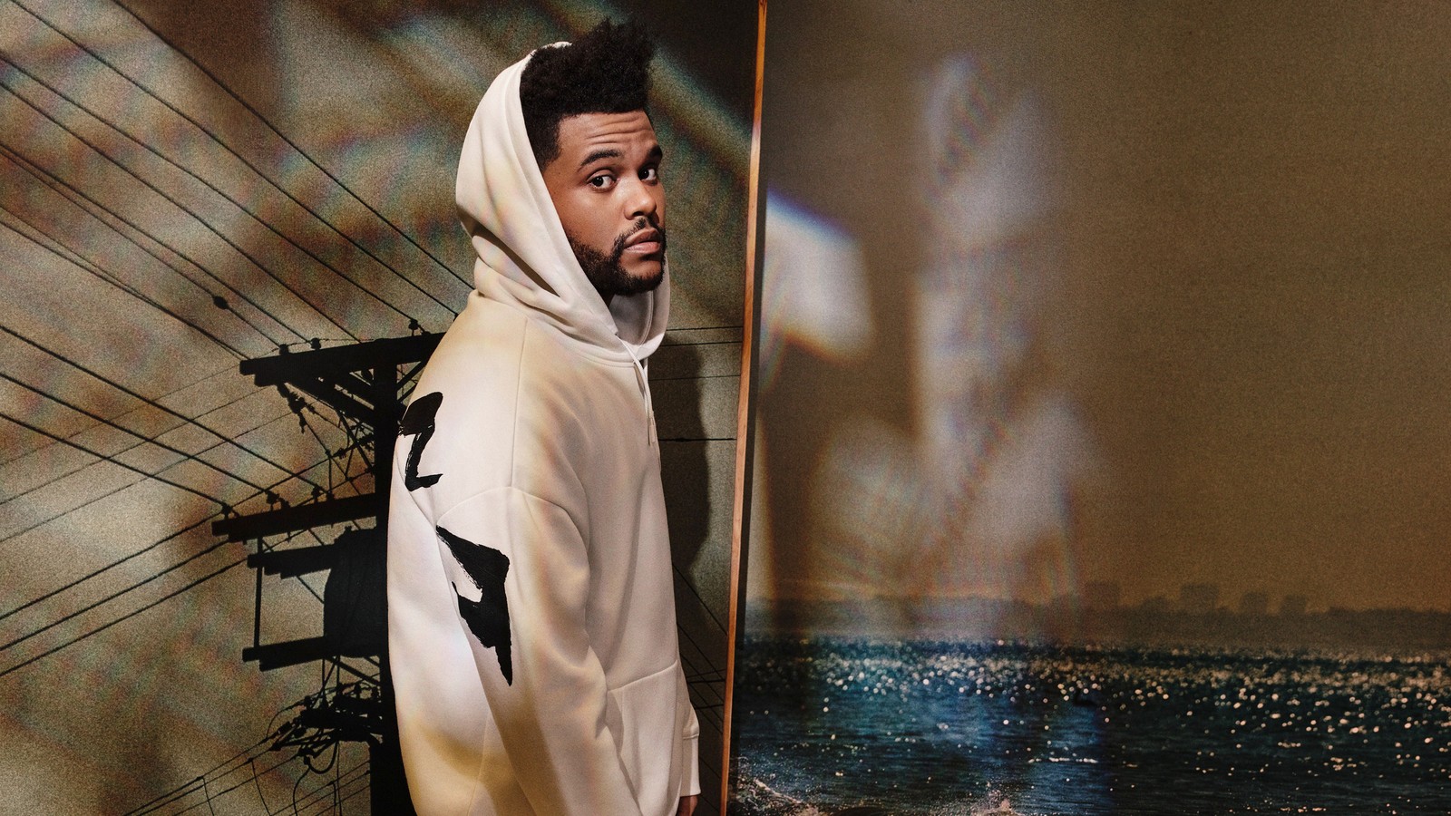 Un homme barbu en sweat à capuche blanc se tient devant une peinture. (the weeknd, sweat à capuche, mode, vêtements dextérieur, vêtements)