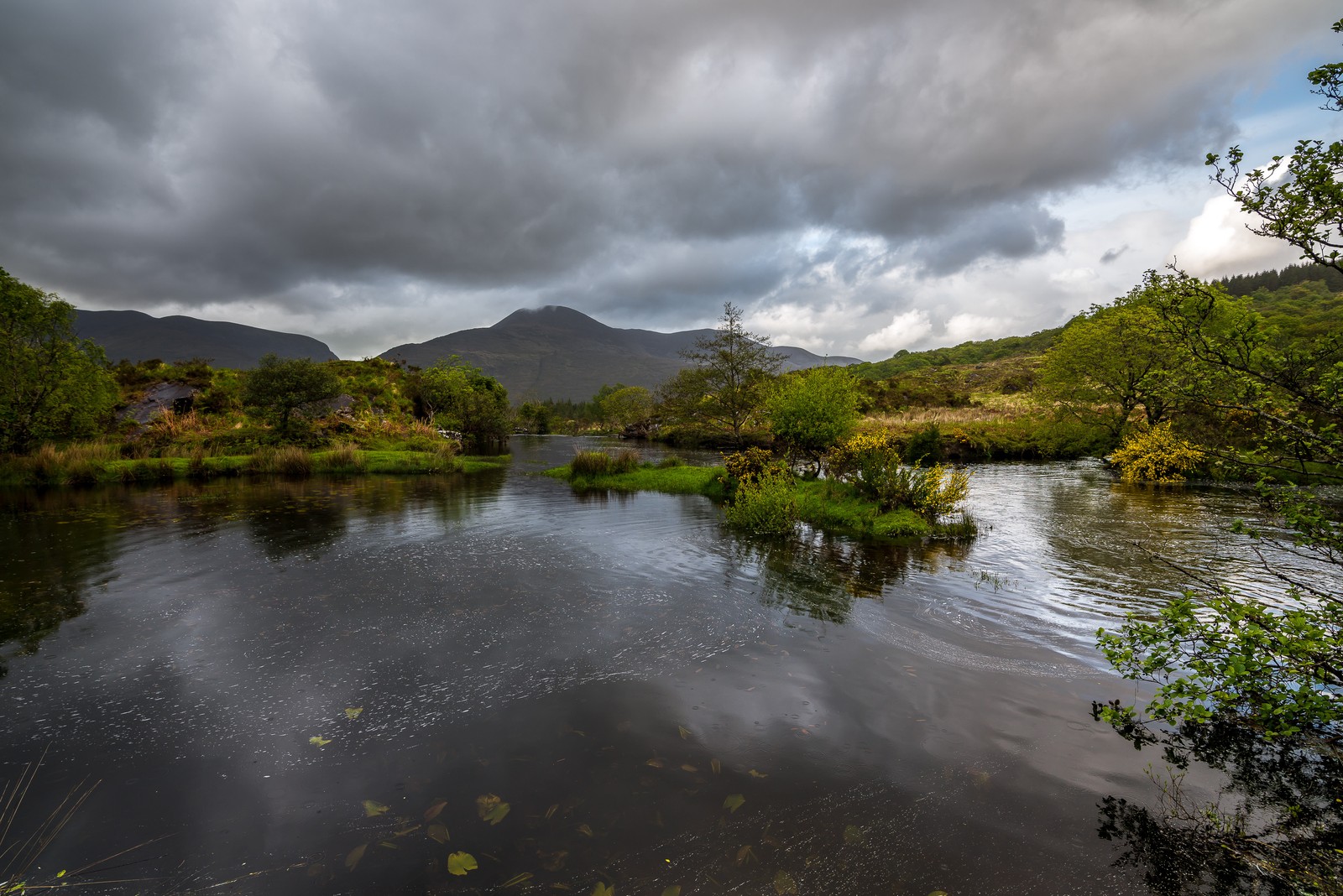 There is a river with a small boat in it and mountains in the background (lake district, body of water, nature, river, water)