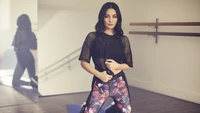 Vanessa Hudgens dans des vêtements de sport élégants, affichant une pose confiante dans un studio de danse.