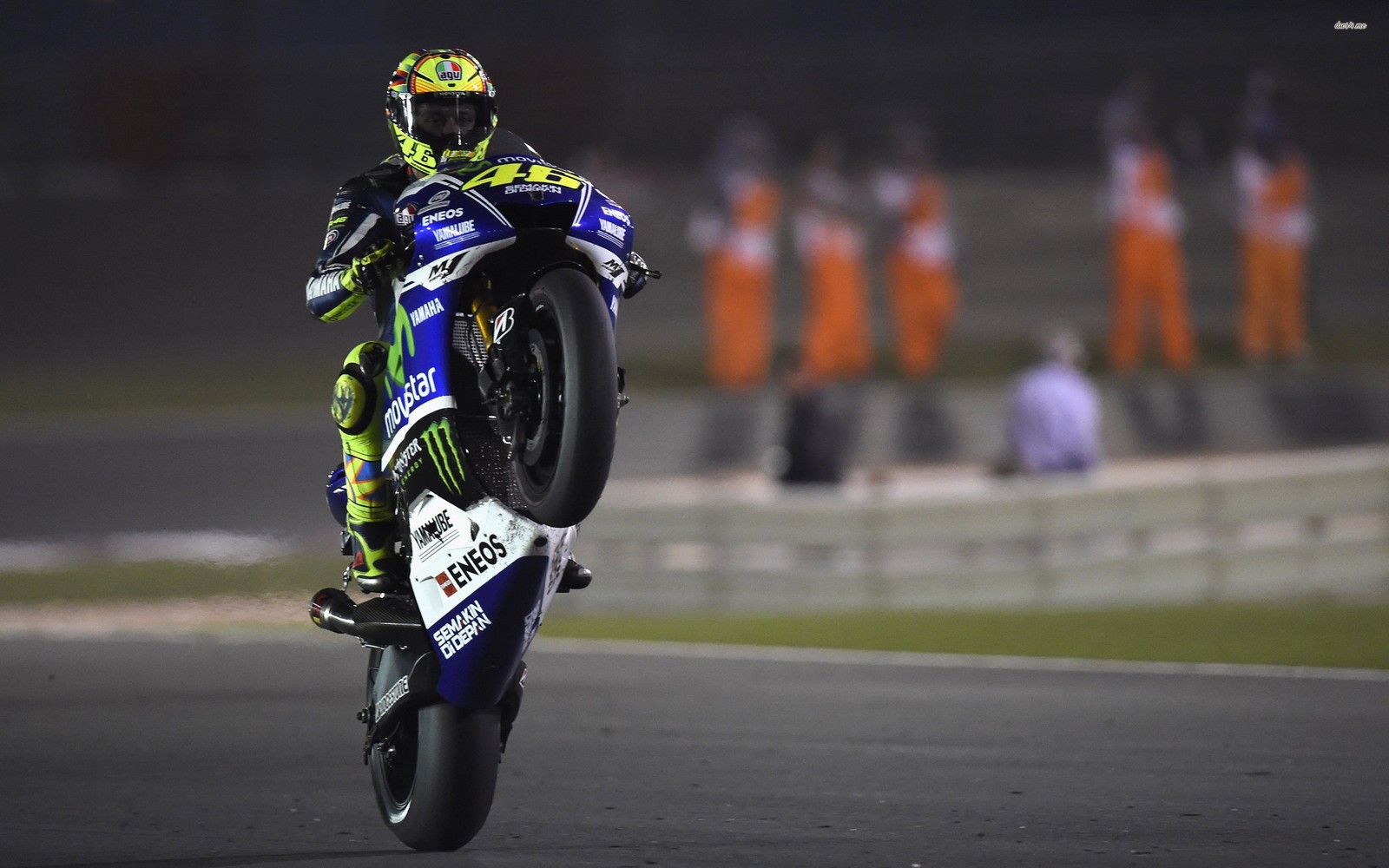 Un motociclista haciendo un caballito en una pista de noche (valentino rossi, valle 46, rossi 46, rossi motogp)