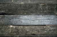 Weathered wooden planks with a rustic texture and faded paint, contrasting against a backdrop of stone brickwork.