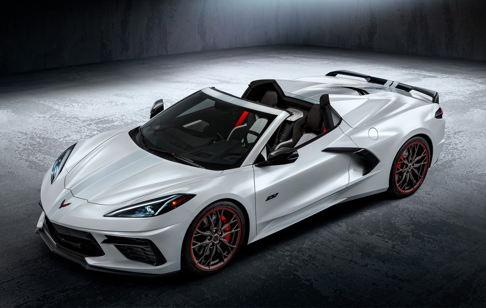 A white corvette convertible car with red accents parked in a dark room (chevrolet corvette stingray, 70th anniversary, convertible, 2023, 5k)