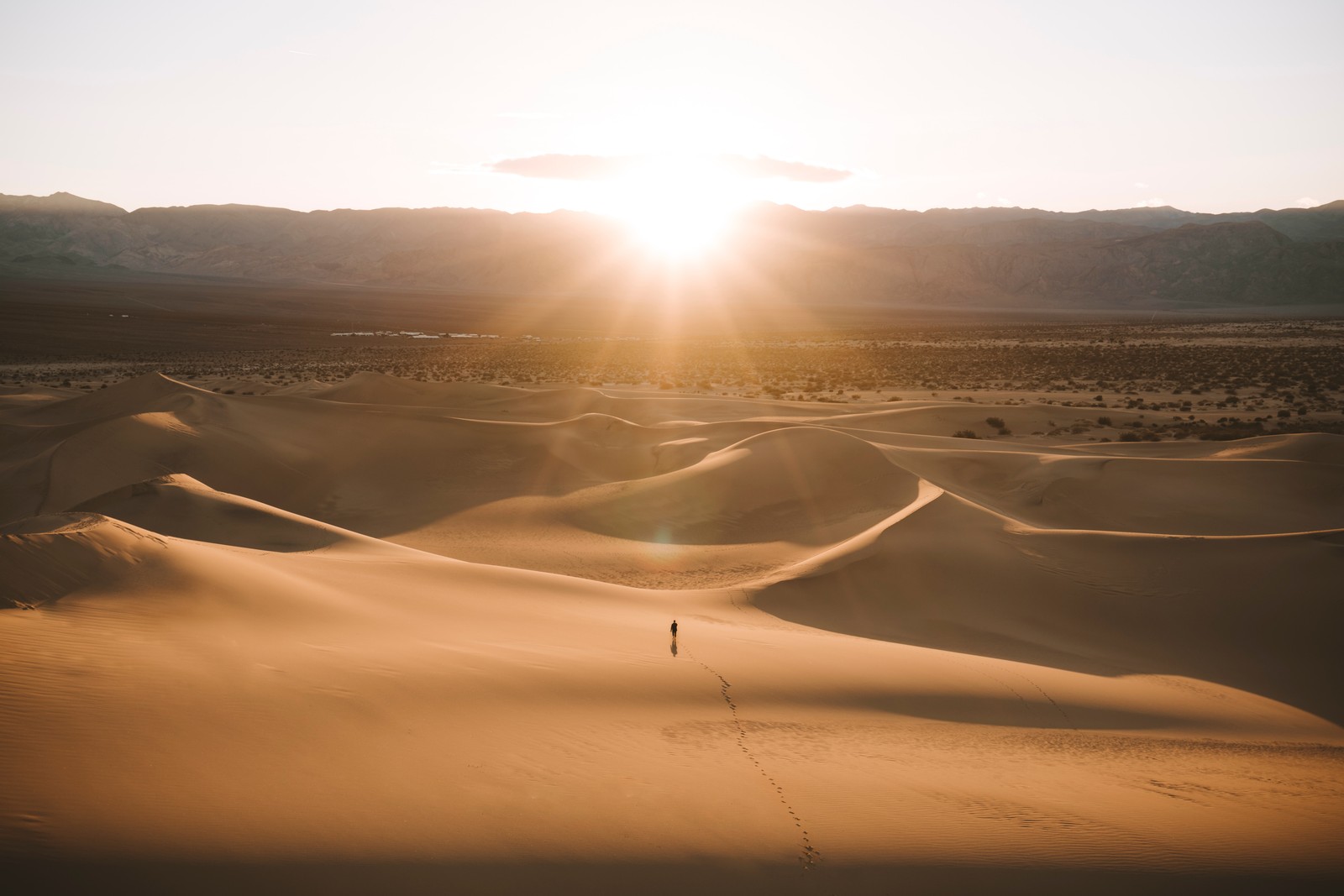 Homem árabe caminhando por um deserto com um pôr do sol ao fundo (saara, sahara, areia, paisagem, luz)