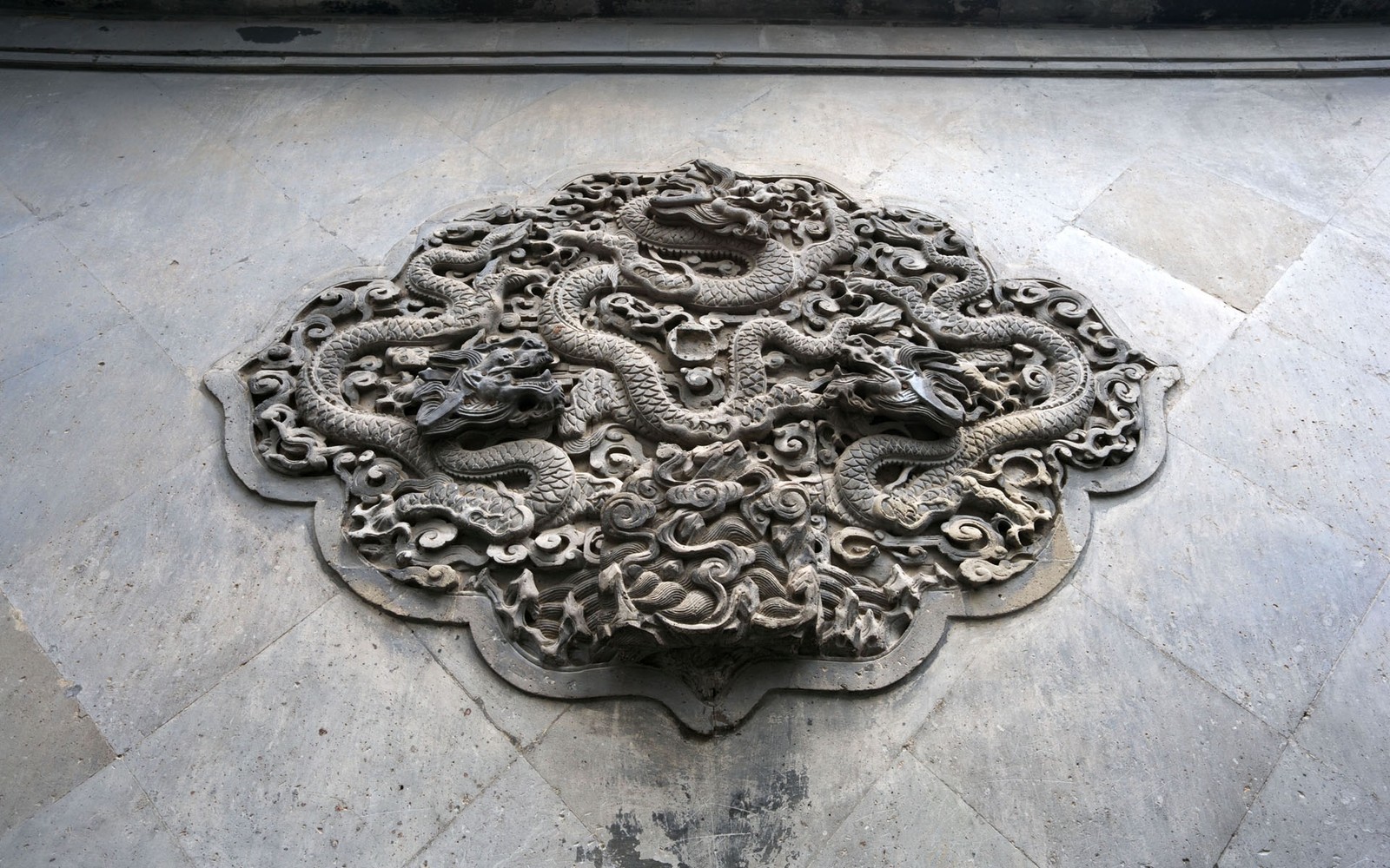 Il y a une sculpture en pierre d'un dragon et d'un serpent sur le sol (dragon, chine, sculpture sur pierre, soulagement, métal)