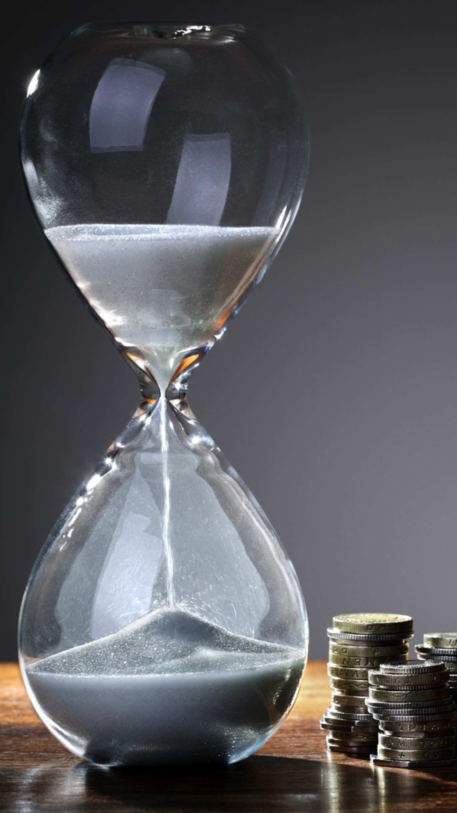 A close up of a hourglass with coins on a table (hourglass, time)