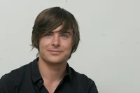 Zac Efron mit stylischen langen braunen Haaren und einem charmanten Lächeln.