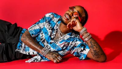 Rapper elegante descansando en una vibrante camiseta gráfica azul contra un fondo rojo audaz, mostrando una moda y gafas únicas.