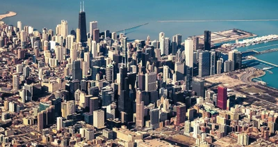 Eine atemberaubende Luftaufnahme der Skyline von Chicago, die seine hohen Wolkenkratzer vor einem klaren blauen Himmel und den schimmernden Gewässern des Michigansees zeigt.