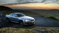 Nissan Skyline GT-R em uma estrada montanhosa cênica ao pôr do sol.