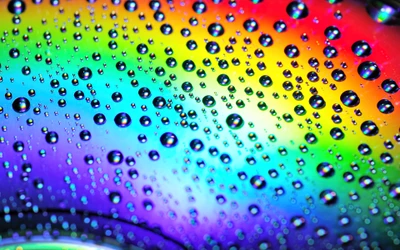 Photographie macro de gouttes d'eau colorées sur un fond arc-en-ciel