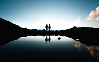 Silhouette eines Paares, das sich an einem ruhigen See bei Dämmerung die Hände hält und die ruhigen Berge der Schweiz widerspiegelt.