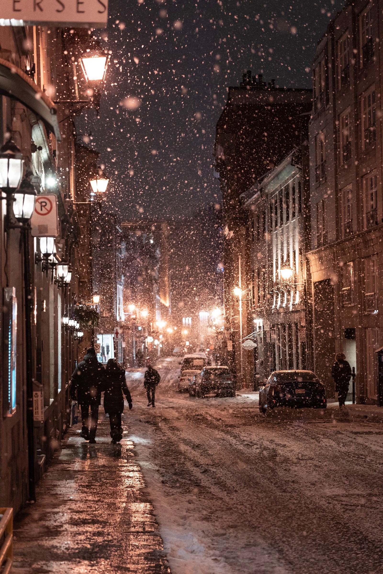 Une scène nocturne enneigée d'une rue de la ville avec des gens marchant dans la neige (neige, hiver, nuit, zone urbaine, réverbère)