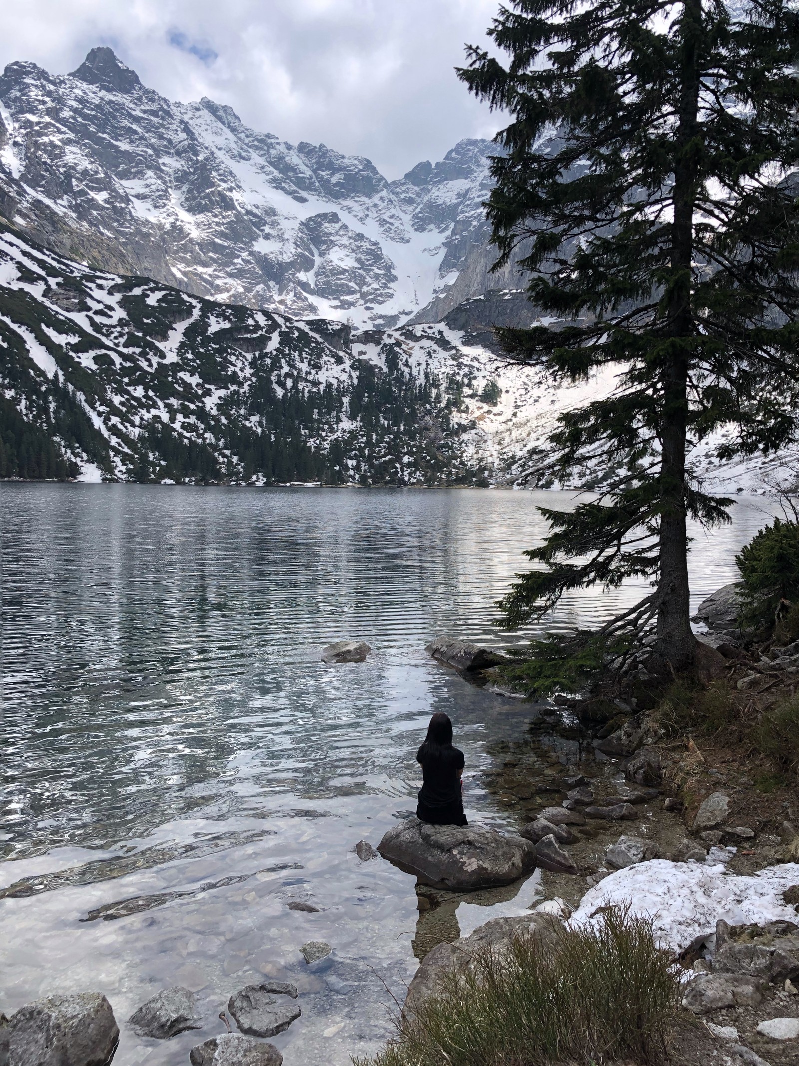 There is a person sitting on a rock by the water (wilderness, mountainous landforms, mountain range, mountain, snow)