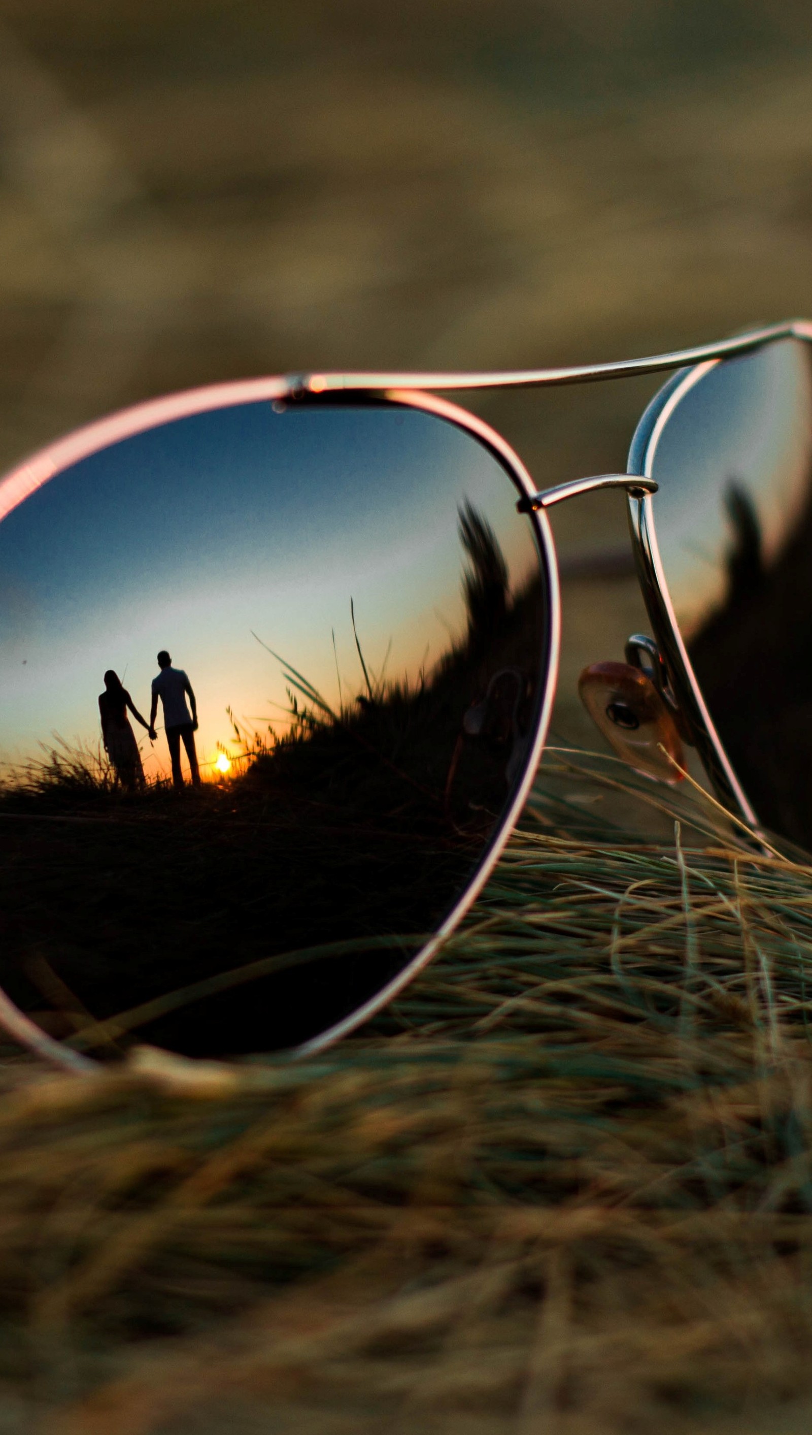 Imagem espelhada de um casal caminhando ao pôr do sol através do reflexo de seus óculos de sol (menino, casal, quadro, menina, vidro)