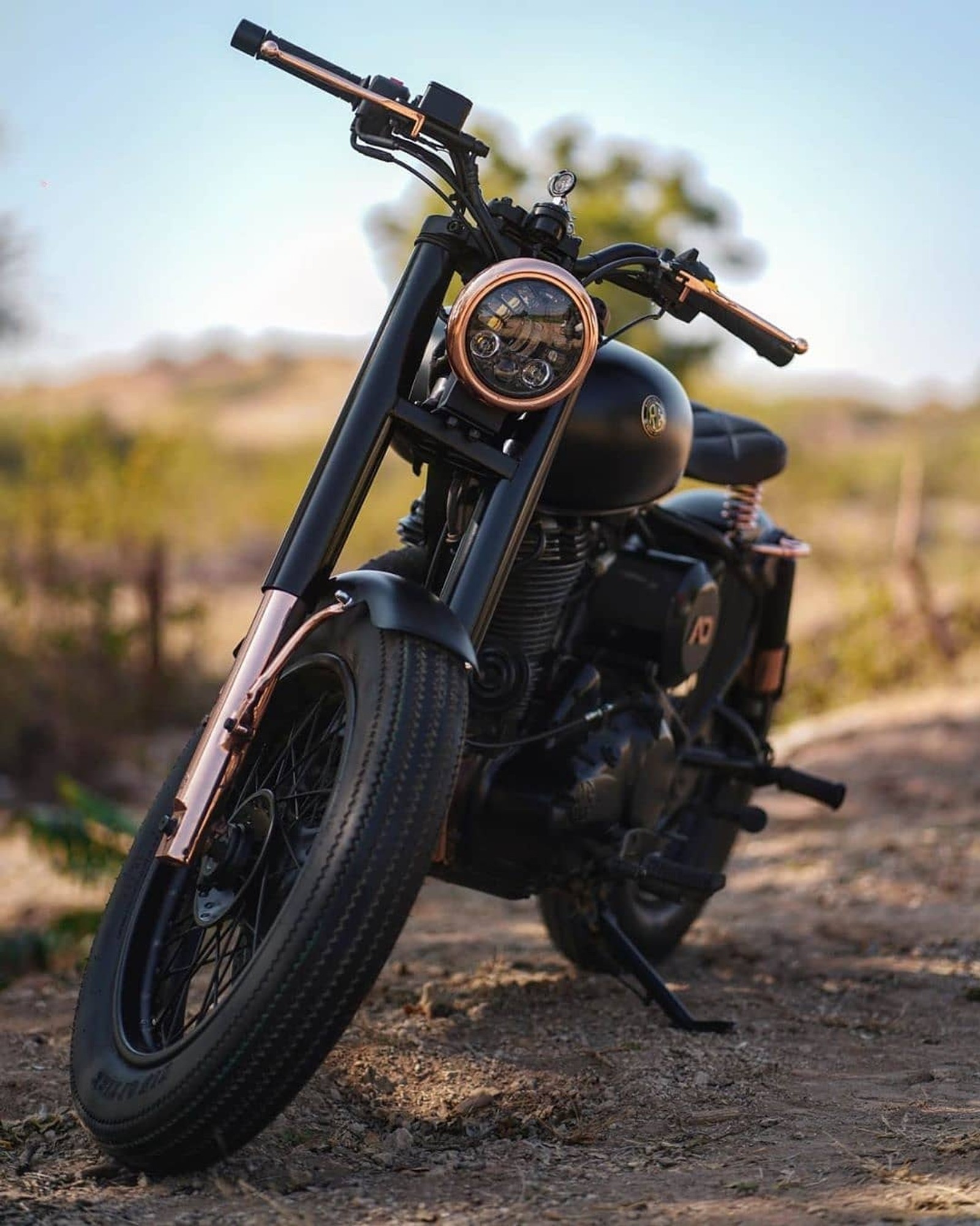 There is a motorcycle parked on the dirt road in the field (bullet, royal enfield)