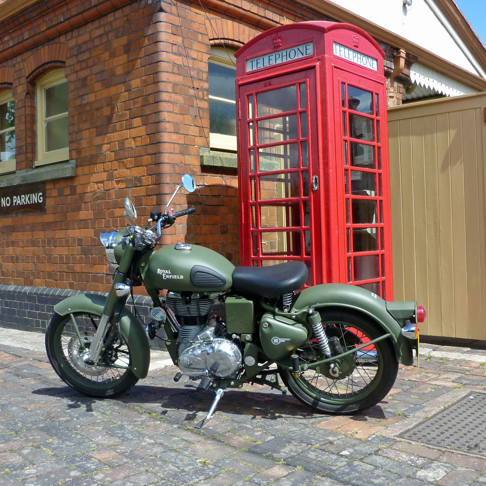 Motorcycle parked in front of a red phone booth next to a brick building (enfield, royal)