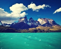 Majestic mountains rise above a vibrant turquoise ocean under a dramatic sky.