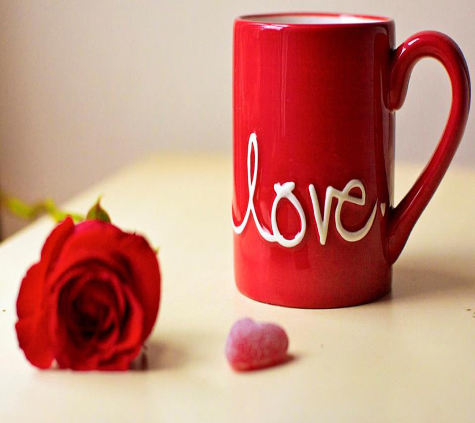 There is a red coffee cup with a rose and candy on the table (love, wallpaper)