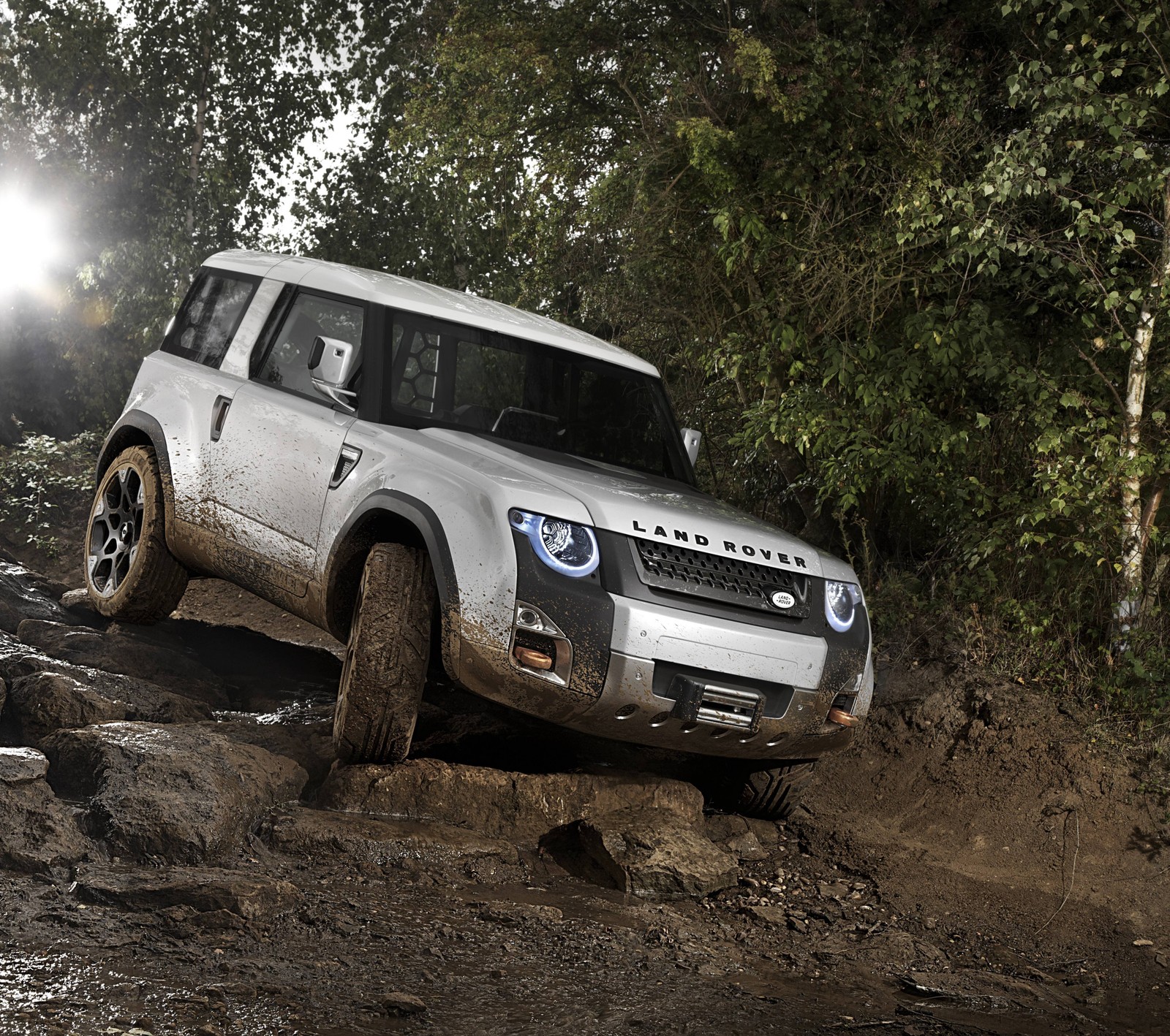 Arafed off road vehicle driving through a muddy area with trees (britain, england, land rover, white)