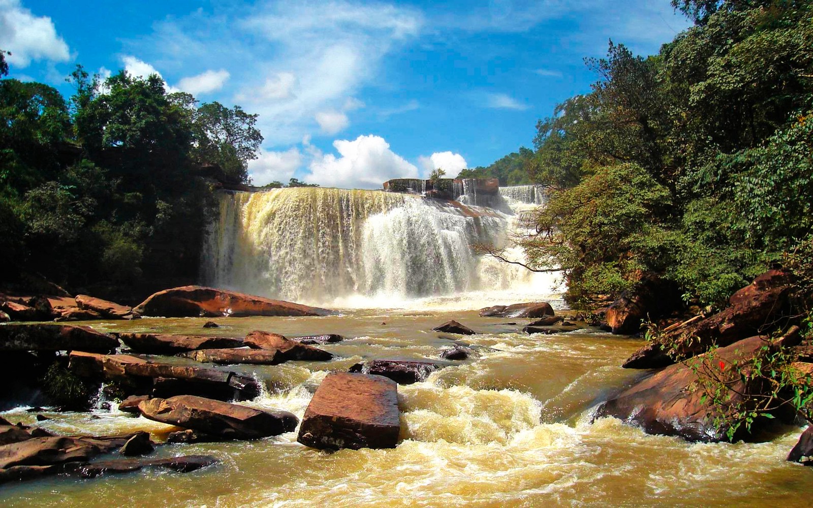 Uma vista de uma cachoeira com algumas pedras em primeiro plano (cachoeira, natureza, recursos hídricos, corpo de água, água)