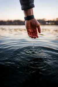 Silhouette of a hand gently dipping into rippling water at sunset.