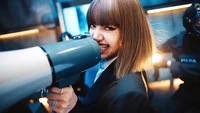 Lalisa Manoban segura um megafone com confiança, exalando carisma e energia em meio a uma cena dinâmica.