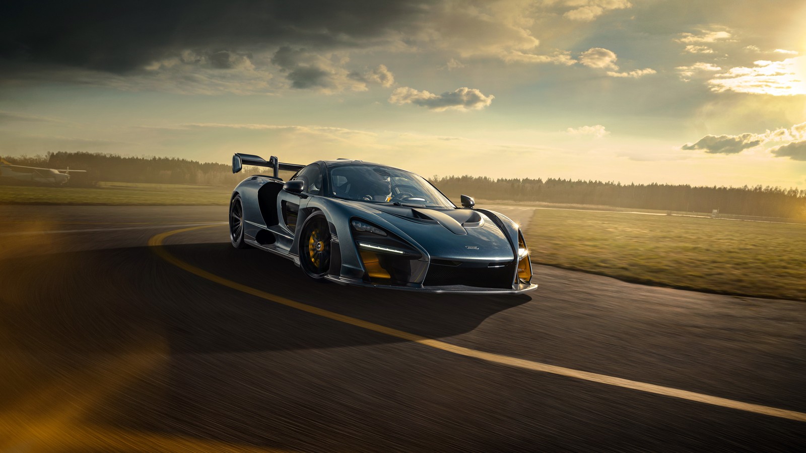 A blue sports car driving down a road with the sun shining behind it (mclaren senna, mclaren, cars, sports car, mclaren automotive)