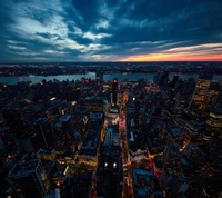 Aerial view of Manhattan skyline at twilight, showcasing vibrant city lights and the Hudson River.