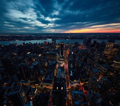 Vue aérienne de la skyline de Manhattan au crépuscule, mettant en valeur les lumières vives de la ville et le fleuve Hudson.