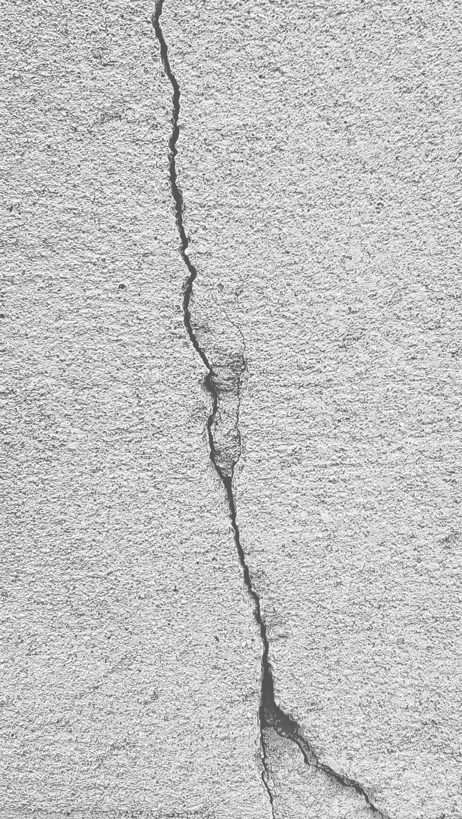 A close up of a crack in the concrete wall of a building (crack, grey, monochrome, simple, wall)