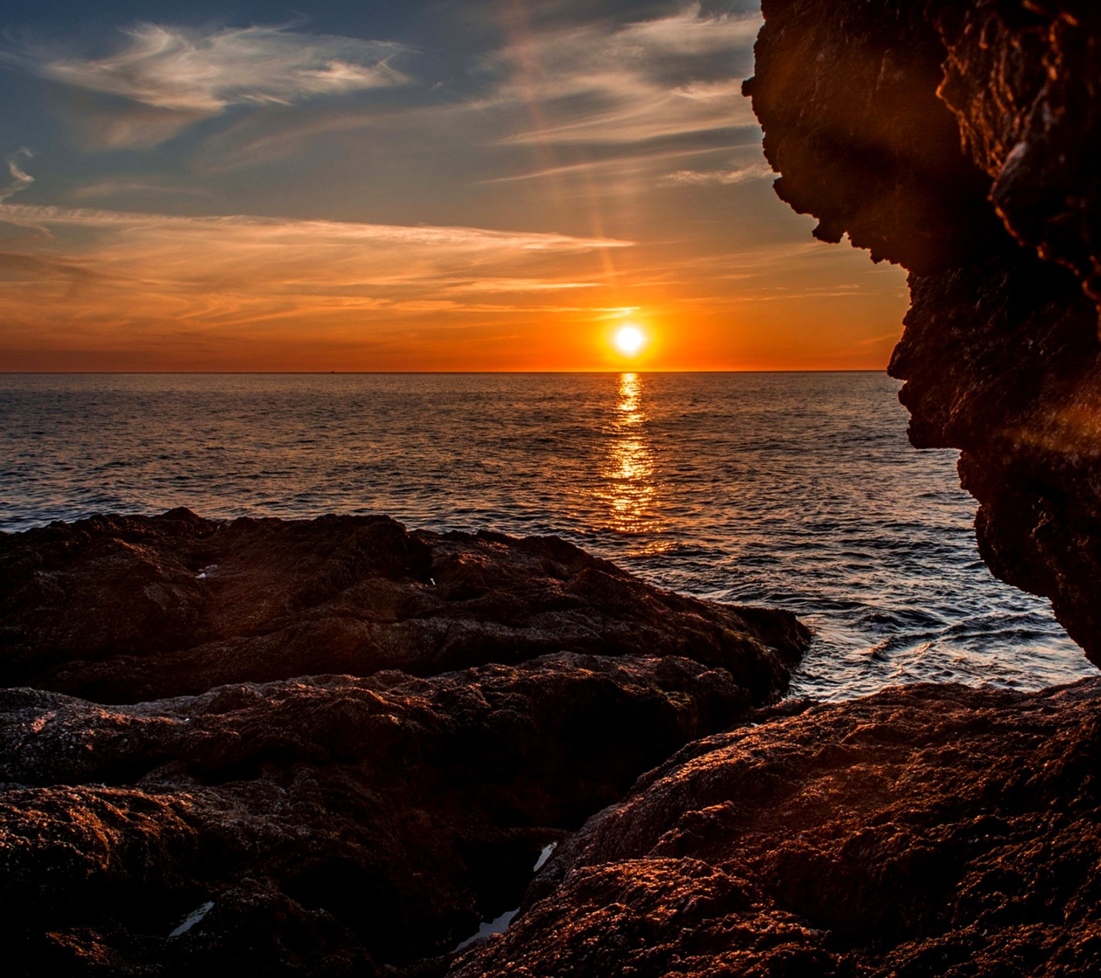 Vista árabe de una puesta de sol sobre el océano con una formación rochosa (playa, impresionante, majestuoso, mar, atardecer)