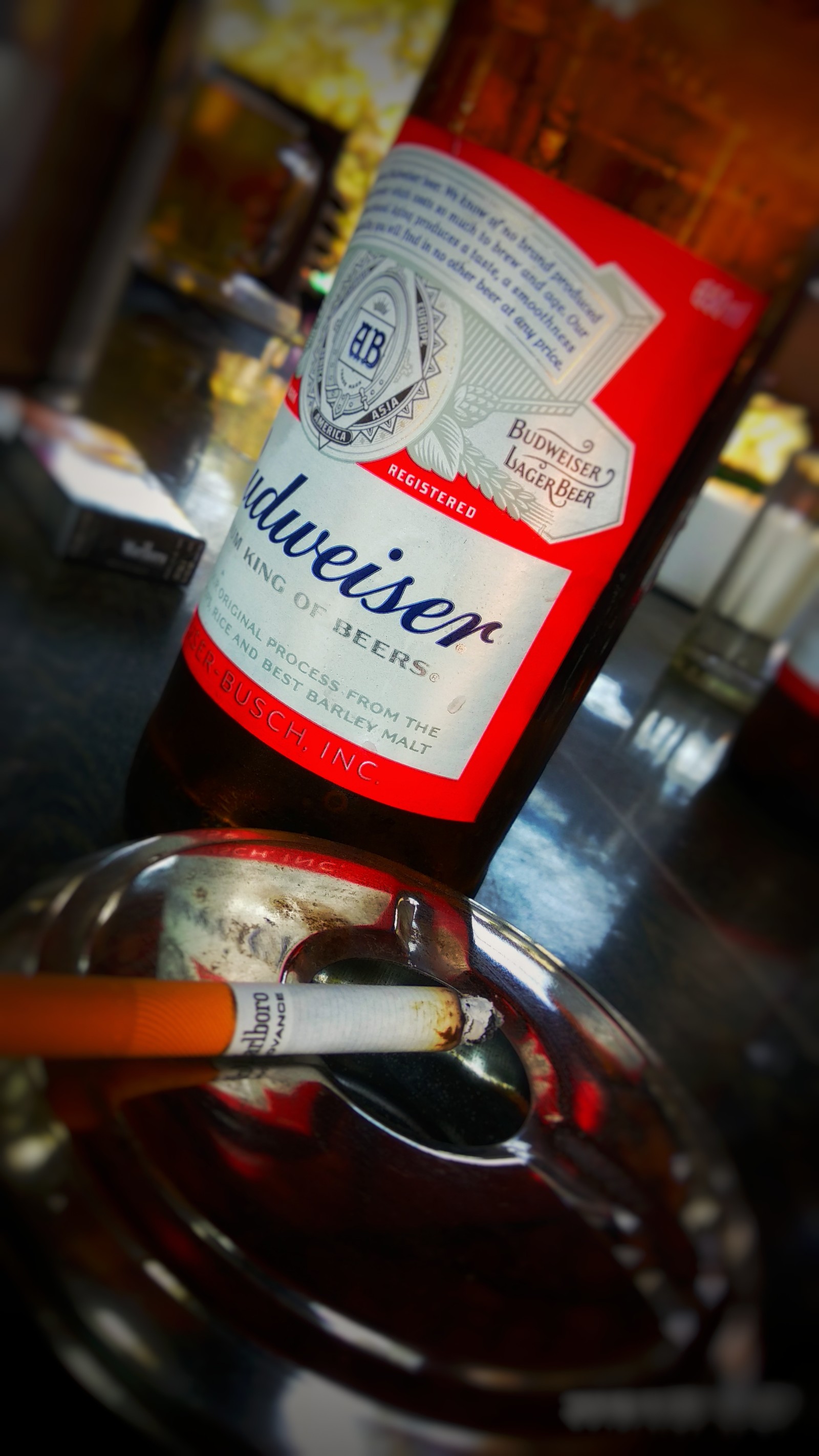 Há um cigarro e uma garrafa de cerveja em uma mesa (cerveja, rei, fumaça)