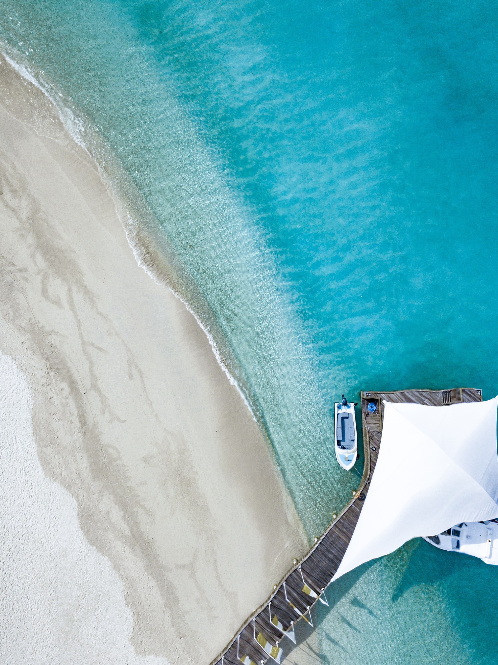 Aerial view of a boat docked on a beach with a white umbrella (blue, turquoise, aqua, teal, azure)