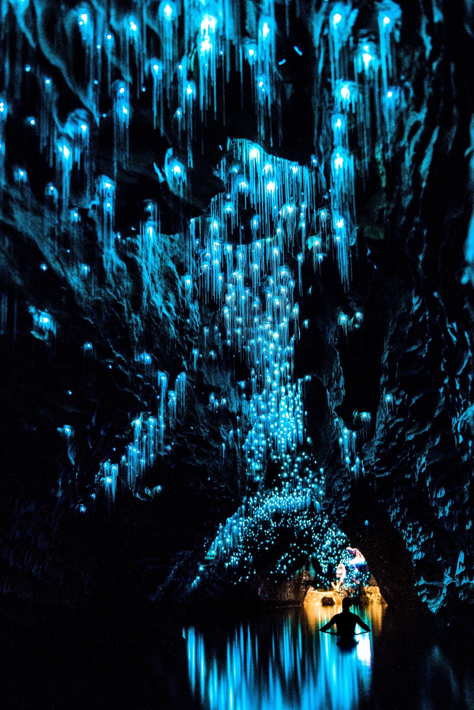 Há um barco flutuando na água com luzes (glowworm, vaga lume, caverna, azul, água)