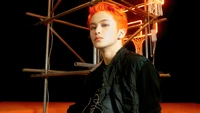 Mark Lee dégage de la confiance avec ses cheveux orange frappants, sur un fond audacieux de lumières néon et de structures industrielles.