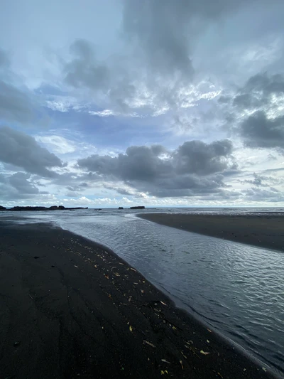 Línea de costa tranquila con arena oscura y nubes tormentosas en Bali