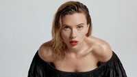 Striking portrait of a woman with tousled hair and bold red lips, exuding confidence in an off-shoulder black outfit against a neutral backdrop.