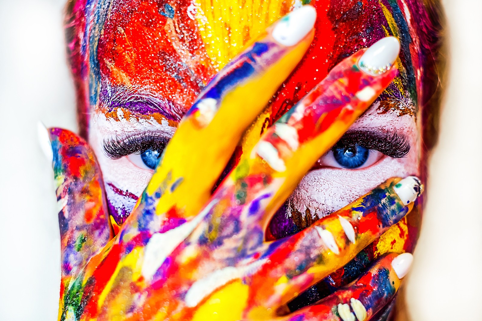 Femme aux couleurs vives avec des mains peintes couvrant son visage de peinture (visage coloré, fille, multicolore, coloré, yeux bleus)