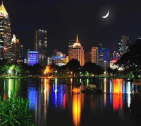 Luces de la ciudad reflejadas en un lago sereno bajo una luna creciente