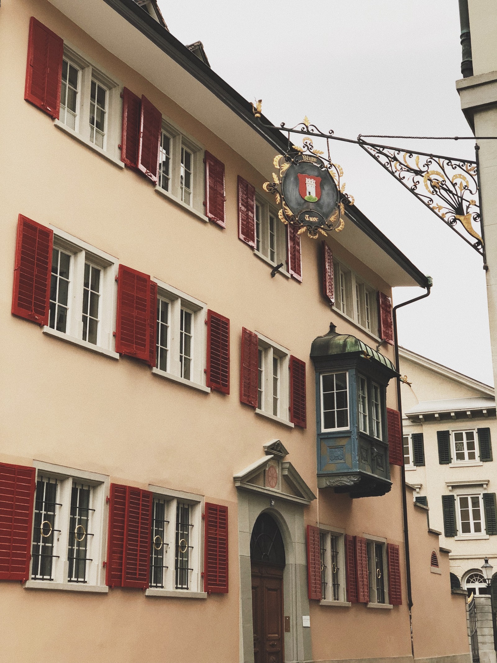 Há um relógio na lateral de um edifício com persianas vermelhas (casa, propriedade, fachada, vizinhança, cidade)