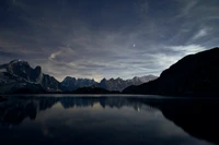 Montanhas majestosas sob um céu estrelado refletidas em um lago tranquilo ao pôr do sol