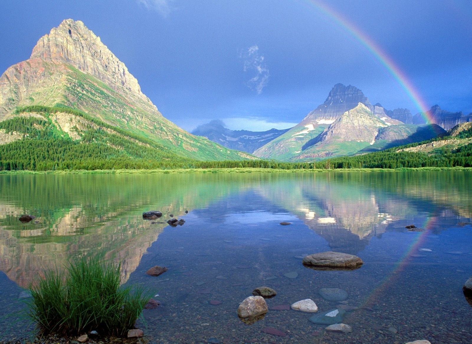 Un gros plan d'un arc-en-ciel au-dessus d'un lac de montagne avec des rochers (paysage, montagnes, nature)